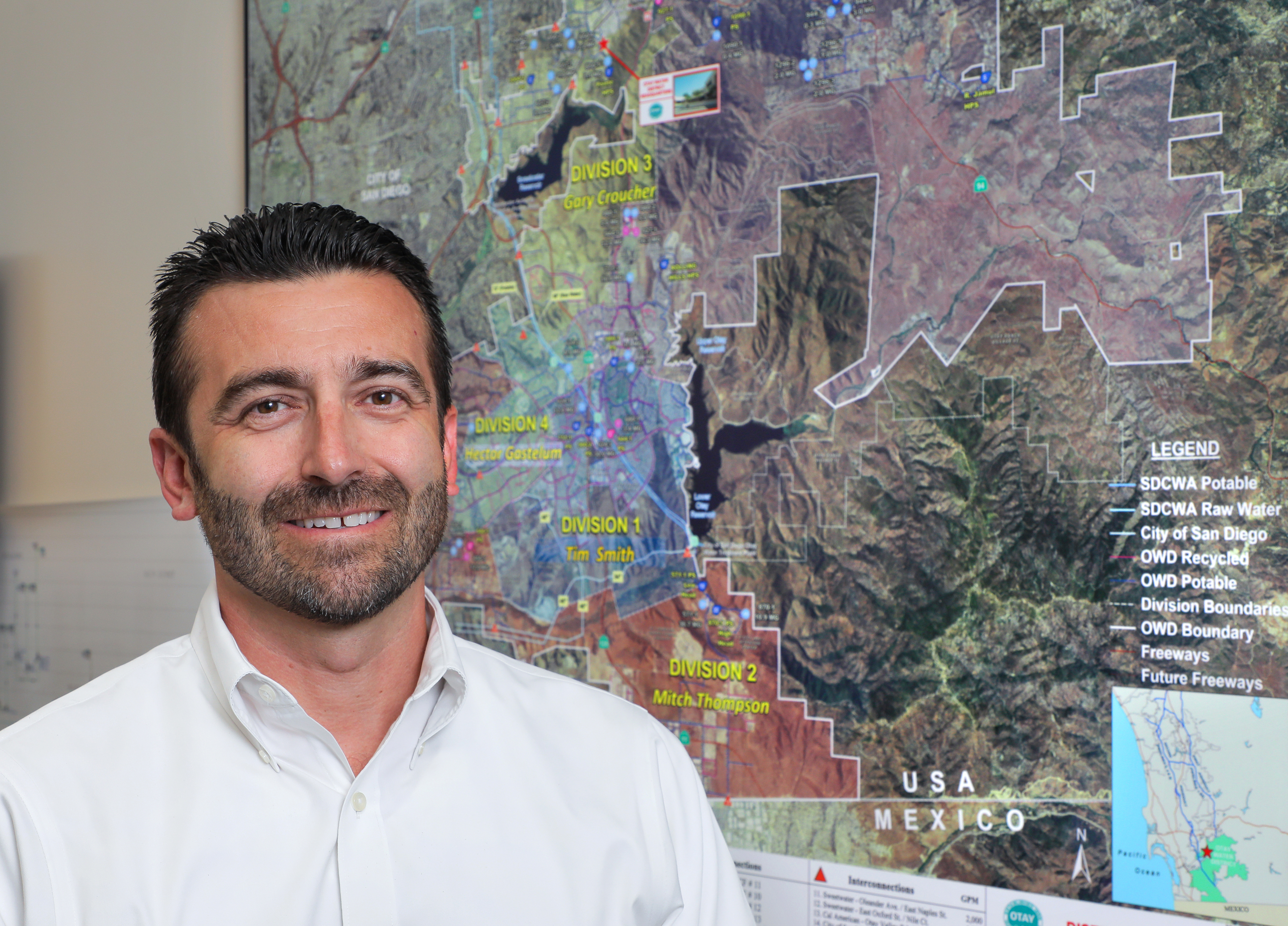 The upper half of a man smiling for the camera with a map behind him.