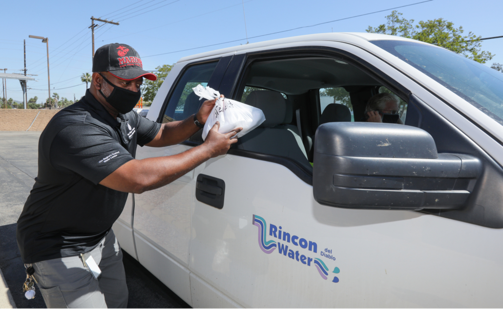 Staff member hands a bag of protective face masks through a car window.
