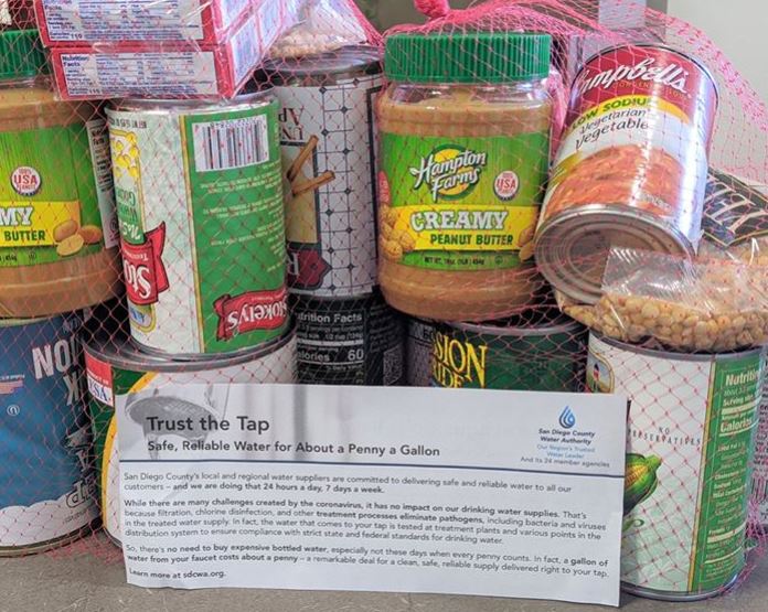A card with information about the safety and reliability of tap water in San Diego County is shown next to jars and cans of food for donation.