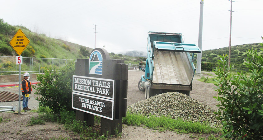 A view of the Mission Trails Regional Park Tierrasanta Entrance sign with a construction worker nearby and a construction truck in the background.