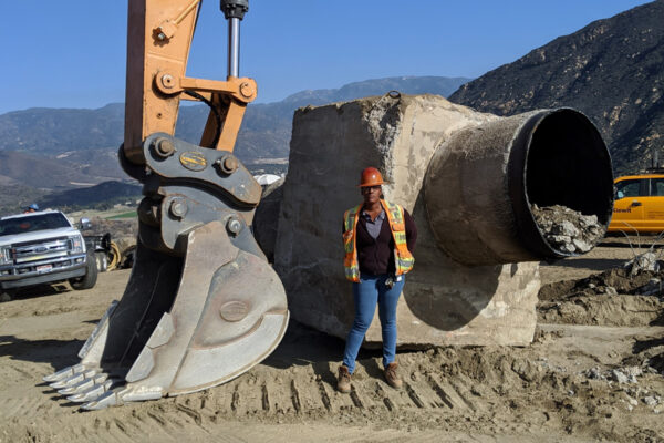 worker standing in front of digger arm and pipeline being built